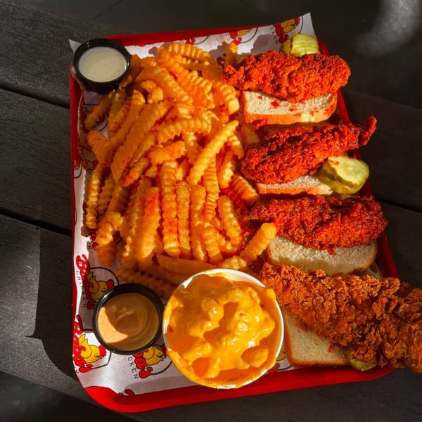 A red tray of Baba's Hot Chicken tenders, crinkle fries, mac and cheese, and dipping sauces.