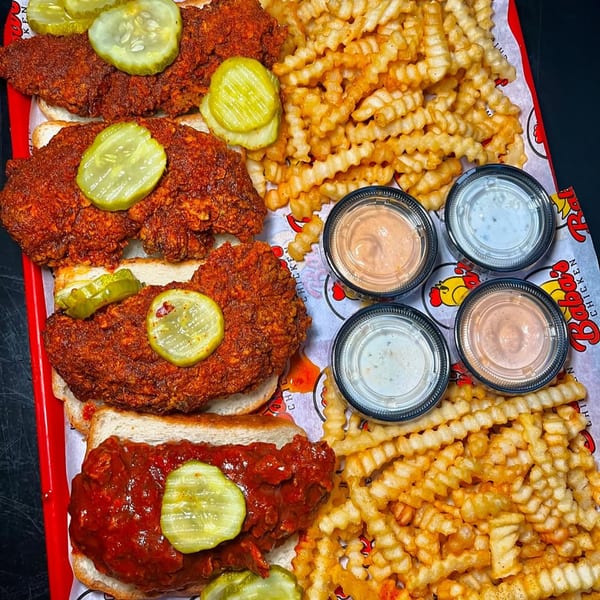 A red tray filled with Baba's Hot Chicken tenders, crinkle-cut fries, and four dipping sauces.
