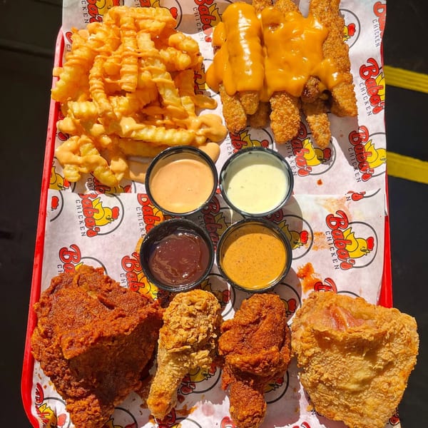A red tray filled with Baba's Hot Chicken, fries, chicken tenders, and four dipping sauces.
