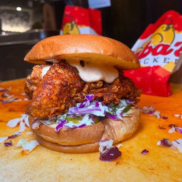 Baba's Hot Chicken sandwich with crispy fried chicken, coleslaw, pickles, and sauce on a bun.