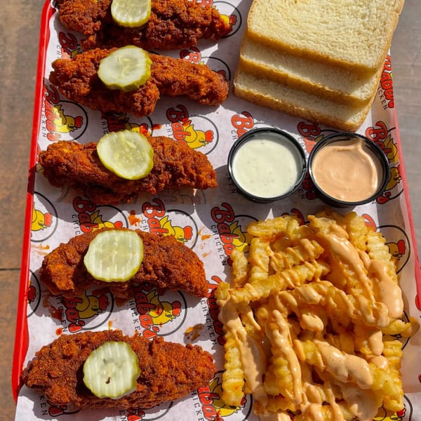 Baba's Hot Chicken tenders with pickles, fries with sauce, white bread, and dipping sauces on a tray.