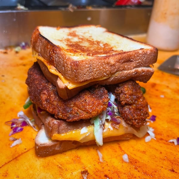 A stacked Baba's Hot Chicken sandwich with fried chicken, cheese, and coleslaw on toasted bread.