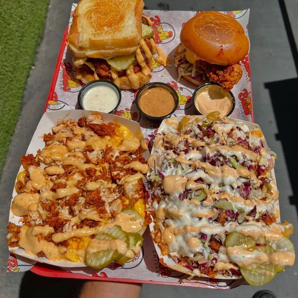 Two Baba's Hot Chicken sandwiches, two loaded fries, and three dipping sauces on a red tray.