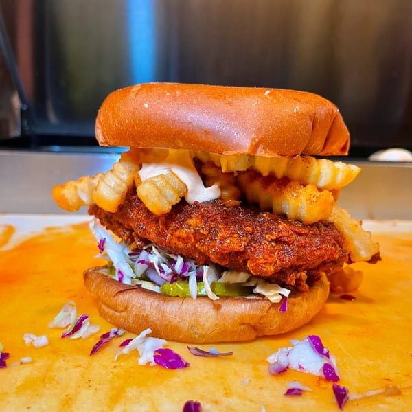 Baba's Hot Chicken sandwich with crispy fried chicken, coleslaw, pickles, fries, and sauce on a bun.
